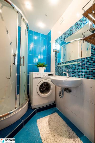 Bathroom with a shower, washing machine, sink, and blue tiles in a 3-room apartment.