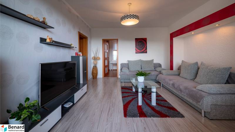 Living room in a 3-room apartment with a gray sofa, glass table, and television.