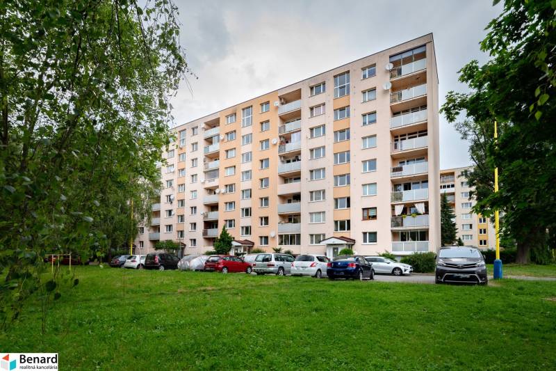 An apartment building on Prostějovská Street in Prešov, surrounded by greenery and parked cars.