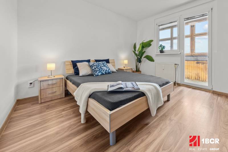 Bedroom with a large bed, nightstand, plant, and a view of the balcony, 3-room apartment.