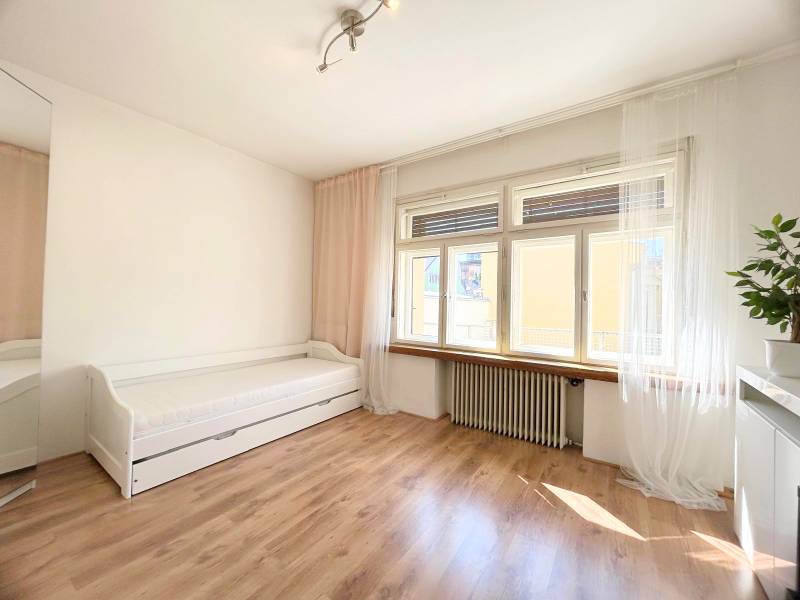 A bright room in a 2-room apartment with simple furniture and a large window.
