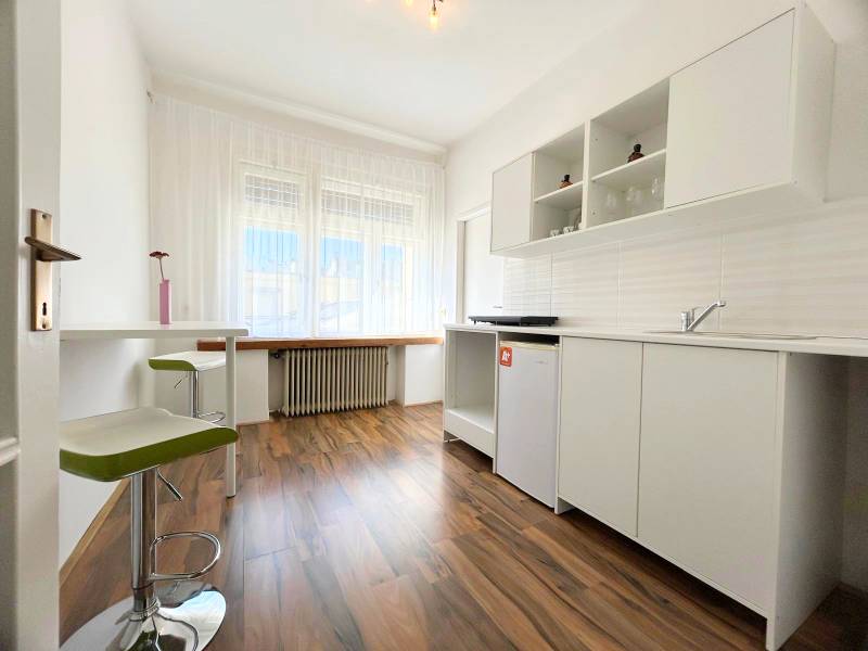 A bright kitchen in a 2-room apartment with laminate flooring and white cabinets.