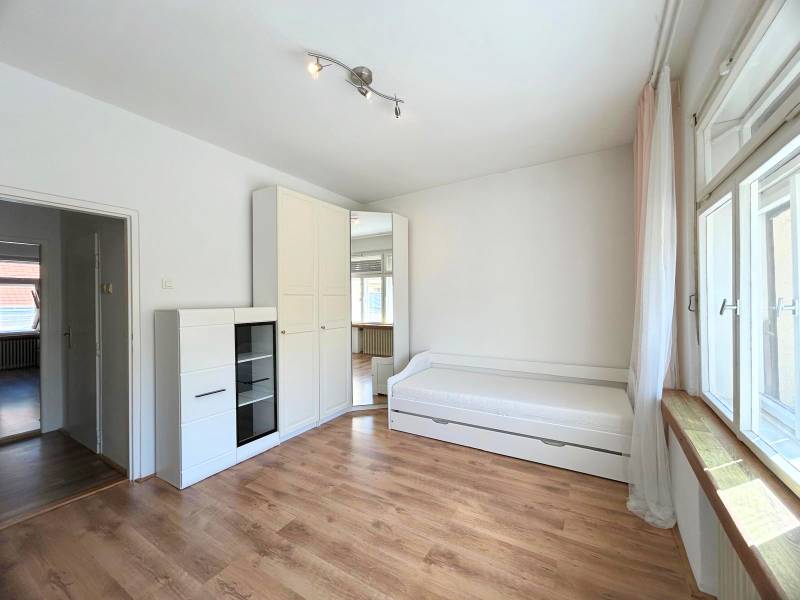 A bright room space in a 2-room apartment with a bed, a cabinet, and a large window.