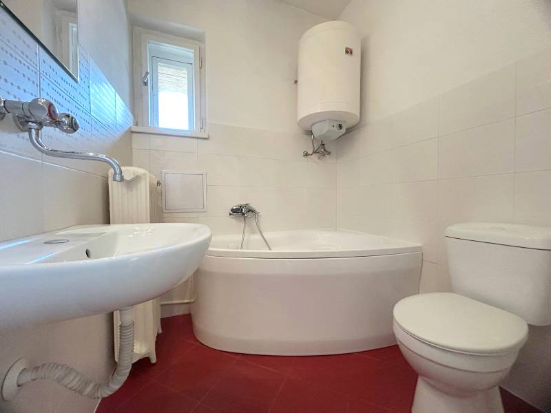 Bathroom with a corner bathtub, sink, toilet, and boiler in a 2-room apartment.