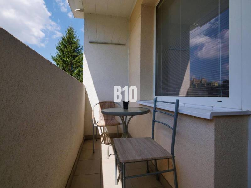 A balcony with two chairs and a table in a studio apartment with a view of a tree.