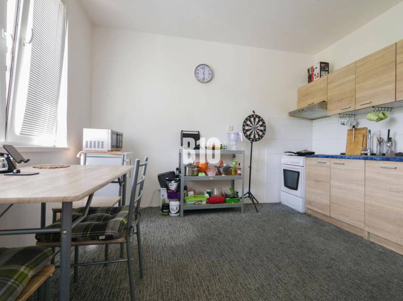 A kitchen in a studio apartment with a dining table, appliances, and a chessboard on the wall.