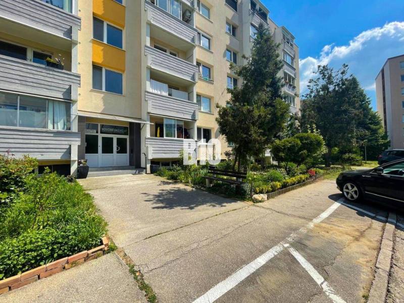 Entrance of an apartment building with parking and greenery in Nitra, suitable for a 1-bedroom apartment.