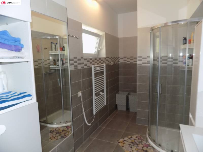 A bathroom in a family house with a corner shower and a shelf with towels.
