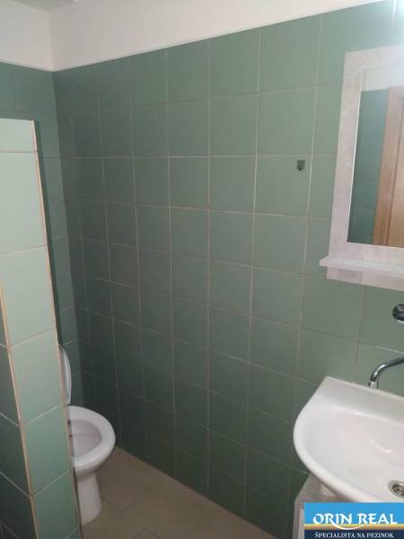 Bathroom of a studio apartment with a sink and toilet, green tiles.