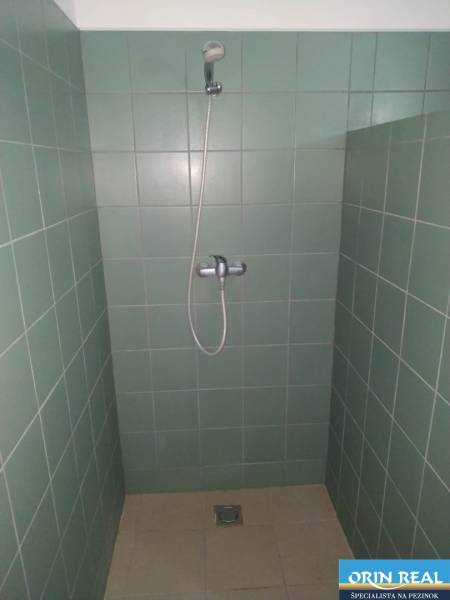A shower corner with green tiles in a studio apartment.