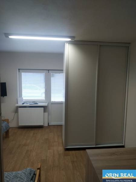 A studio apartment with wooden flooring, a wardrobe, and windows with blinds, ideal for living.