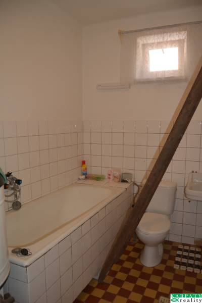 A bathroom with a bathtub and a toilet in a family house, with tiles and wooden stairs.
