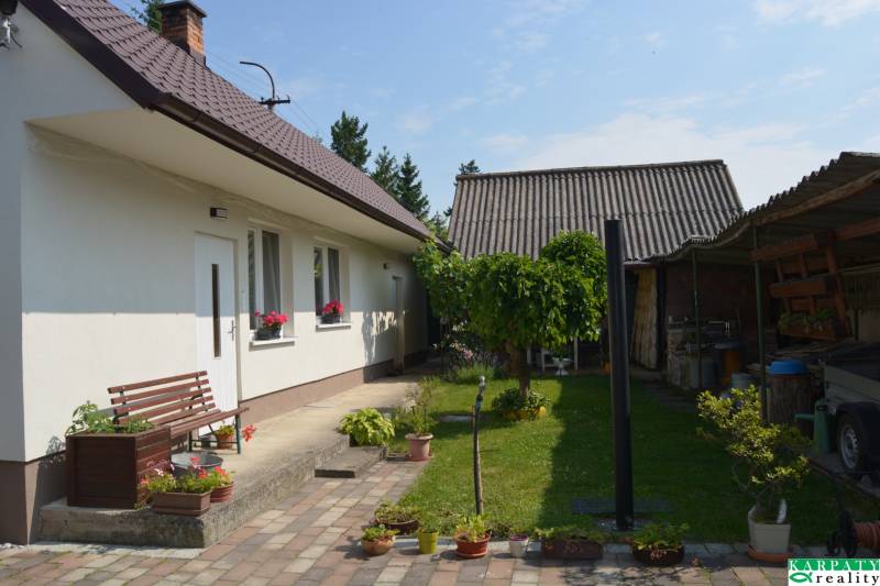 A family house in Trstín with a landscaped garden, a bench, and plant details.