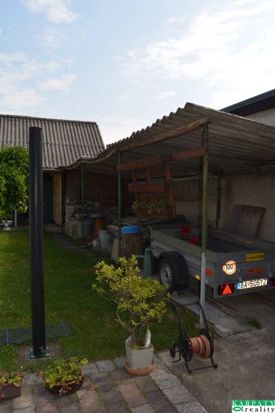 The courtyard of a family house in Trstín with a shelter, a trailer, and plants in pots.