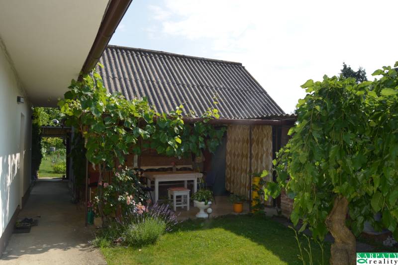 A family house in Trstín with a terrace, a garden table, and lush vegetation.