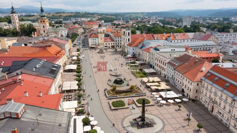In the picture, there is a square in Banská Bystrica with an advertisement for a 1-room apartment.