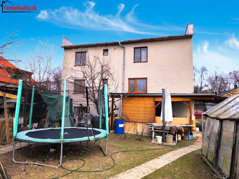 A two-story family house with a trampoline in the garden, a greenhouse, and outdoor seating.