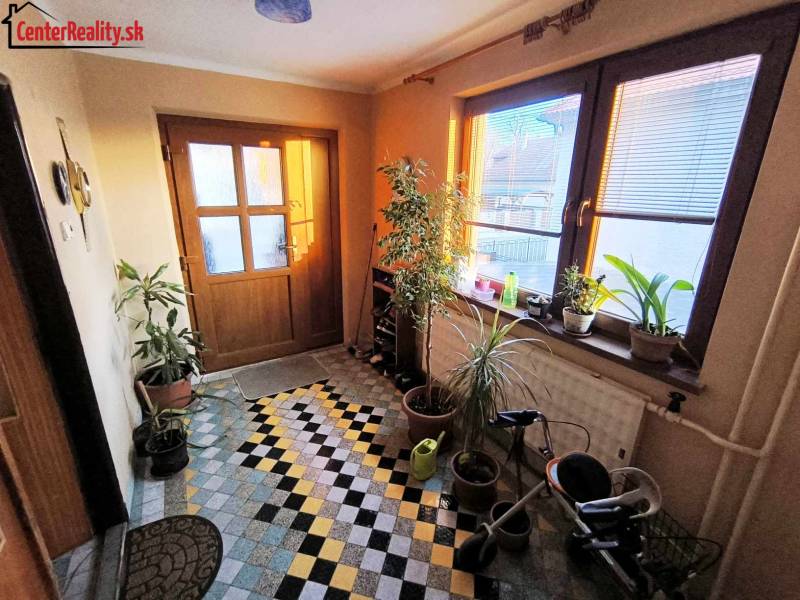 Entrance hall with tiles, plants, a stroller, and light in a family house.