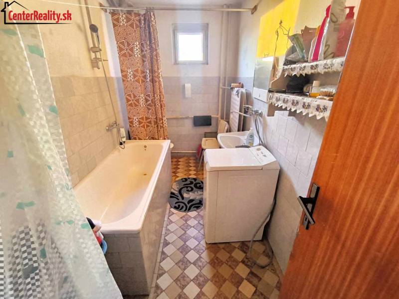 A bathroom with a shower, washing machine, sink, and patterned floor in a family house.