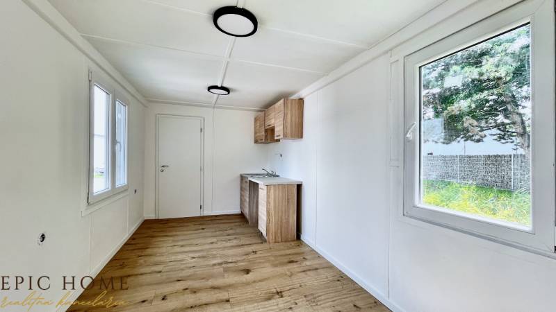 A simple interior with wooden flooring, windows, and a kitchen unit in a cottage.