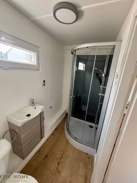 Bathroom in a cabin with a wooden floor, shower corner, and a small sink.