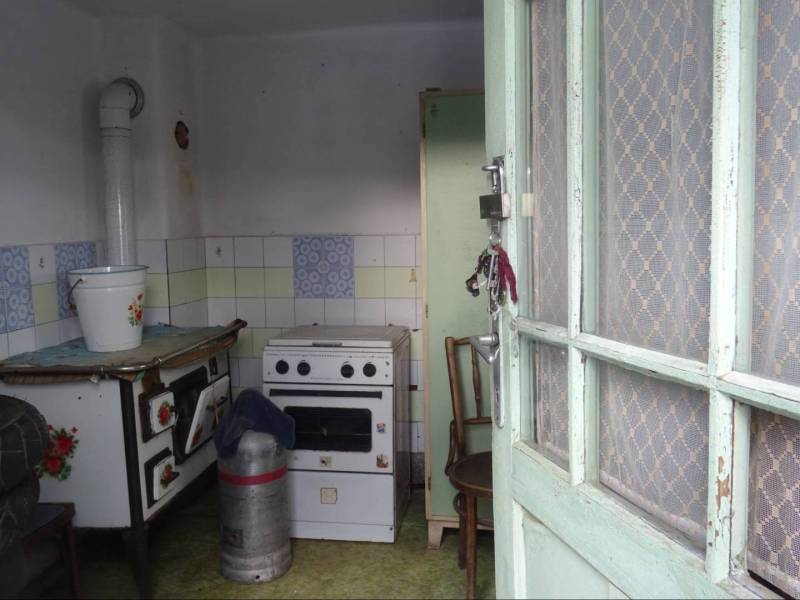 A kitchen in a family house with a stove, a gas cooker, and a bucket on the table.