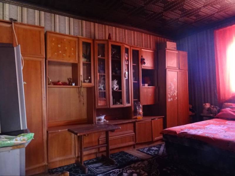 A room in a family house with a wooden wardrobe, a bed, and colorful curtains.