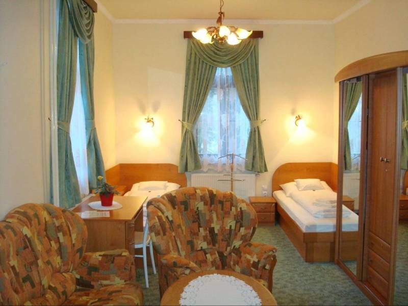 A room in a hotel and guesthouse with beds, chairs, a mirrored wardrobe, and decorative curtains.