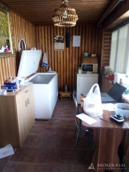 A kitchen in a family house with wooden walls, a freezer, a microwave, a table, and a shelf.