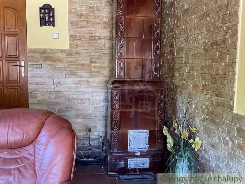 Interior of a family house with a tiled stove, a leather armchair, and stone walls.