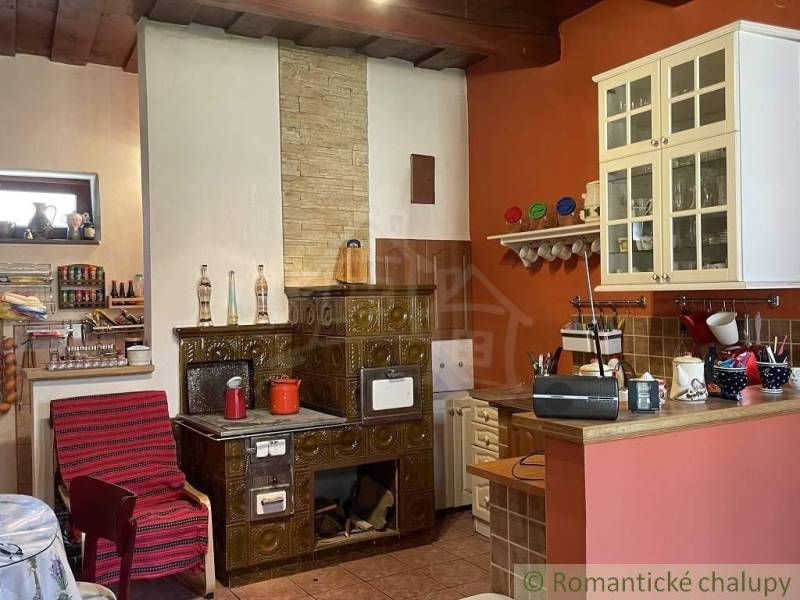 A kitchen in a family house with antique tiles, a wooden ceiling, and a shelf with dishes.