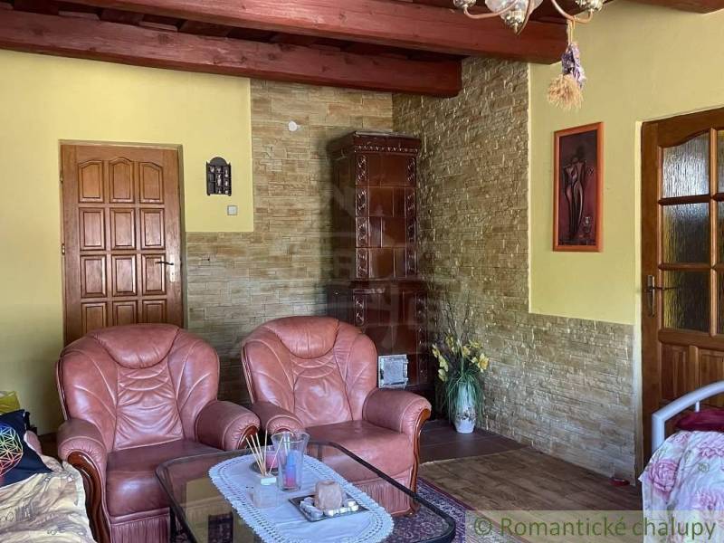 Living room of a family house with leather armchairs, a stove, and wooden ceiling beams.
