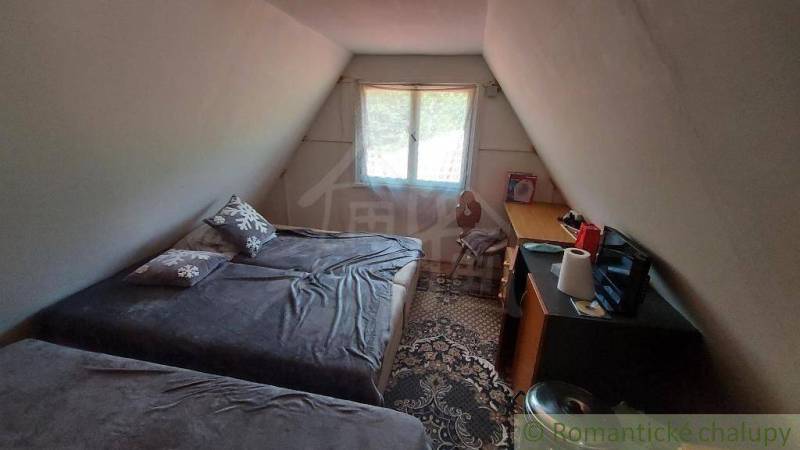 The attic room in the cottage with two beds, a table, and a window exudes coziness.