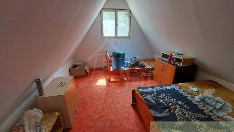An attic room in a cottage with simple furnishings, an orange carpet, and a bed.