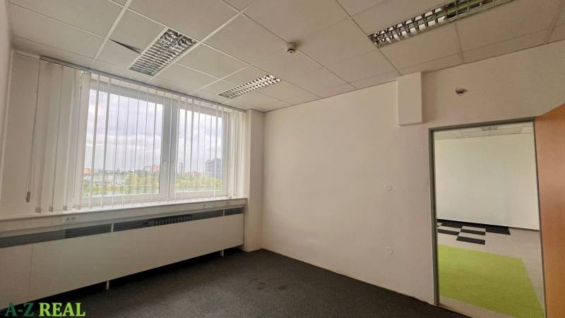 Empty office with carpet, large window, and view into the adjacent room.
