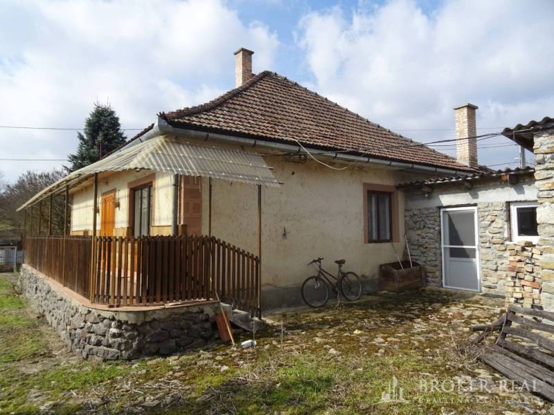 A family house in Füzérkomlós with a gable roof, a stone annex, and a picket fence.