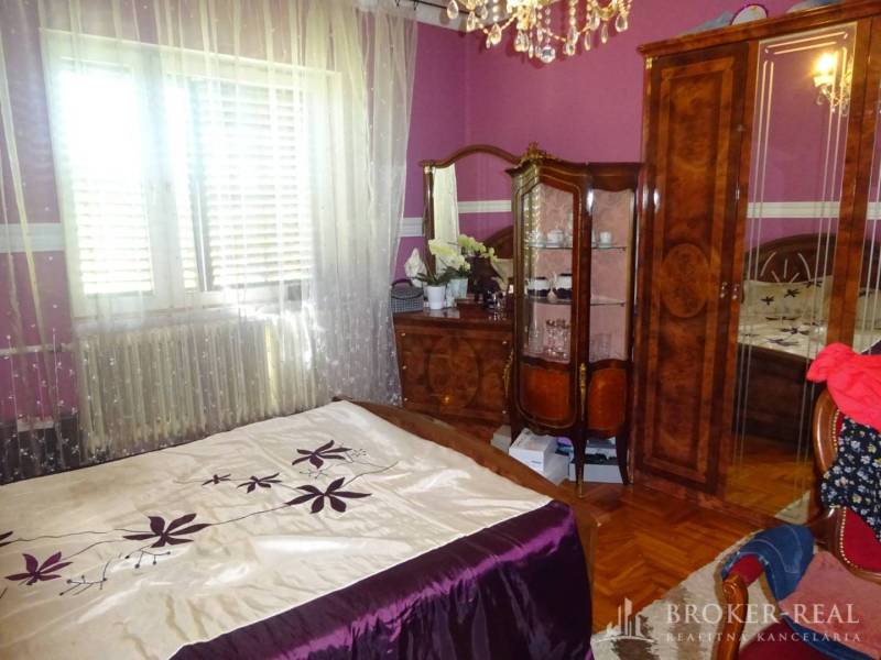 A bedroom in a family house with wooden furniture, purple walls, and decorative curtains.
