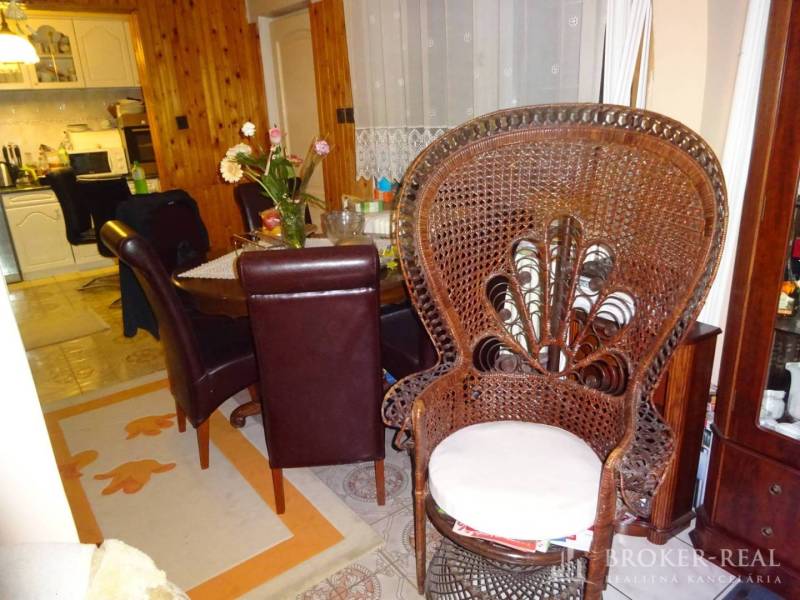 Dining room in a family house with a wicker chair, flowers, and wooden furniture near the kitchen.