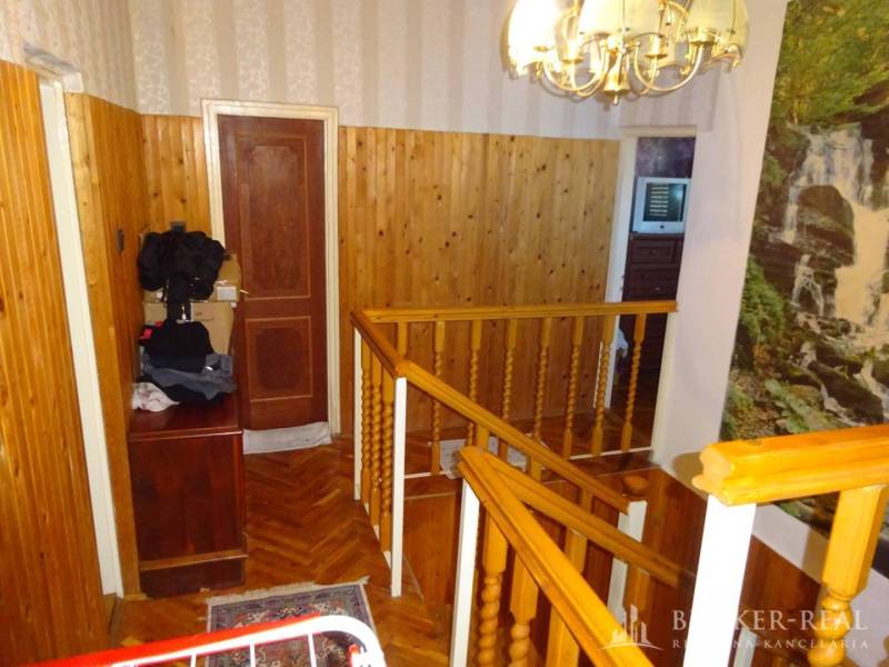 A hallway in a family house with wooden paneling, railing, and stairs, with a painting on the wall.