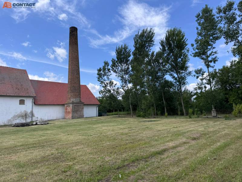 Old brick chimney next to a building in Zemianske Sady, warehouses and halls, surrounded by trees.