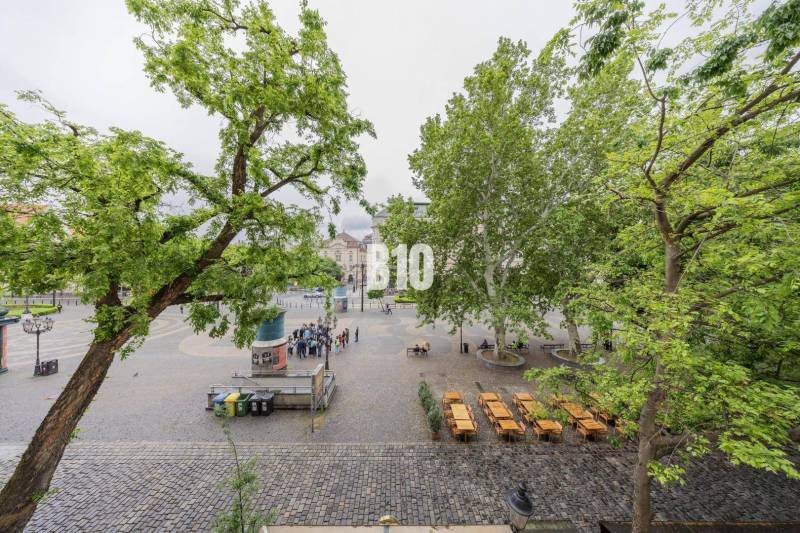 A historic square surrounded by trees with empty café tables, Bratislava - Old Town.