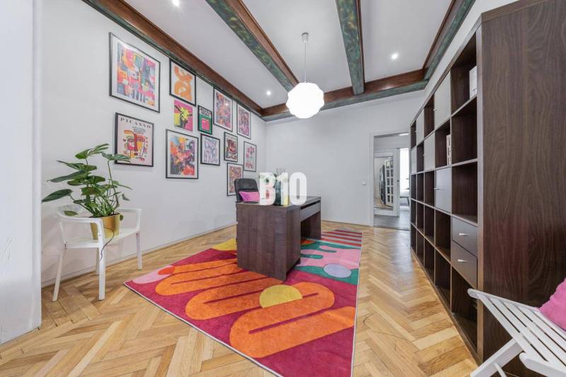 A stylish office in a 2-room apartment with a desk, shelves, and colorful paintings on the wall.