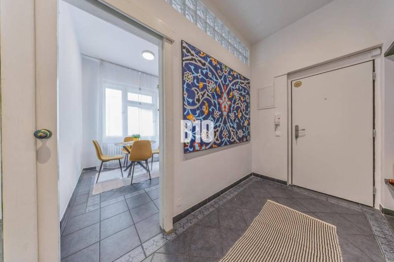 Entrance hall in a 2-room apartment with a colorful painting and a view into the dining room with chairs.