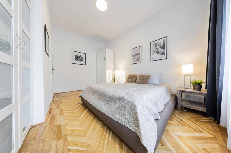 A bedroom in a 2-room apartment with patterned flooring and artistic photographs on the walls.