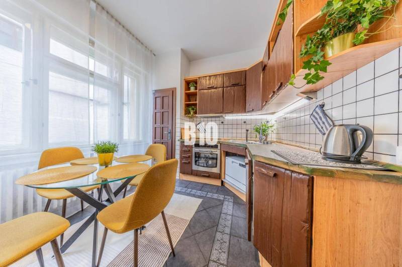 A kitchen in a 2-room apartment with a wooden kitchen unit, a dining table, and light curtains.