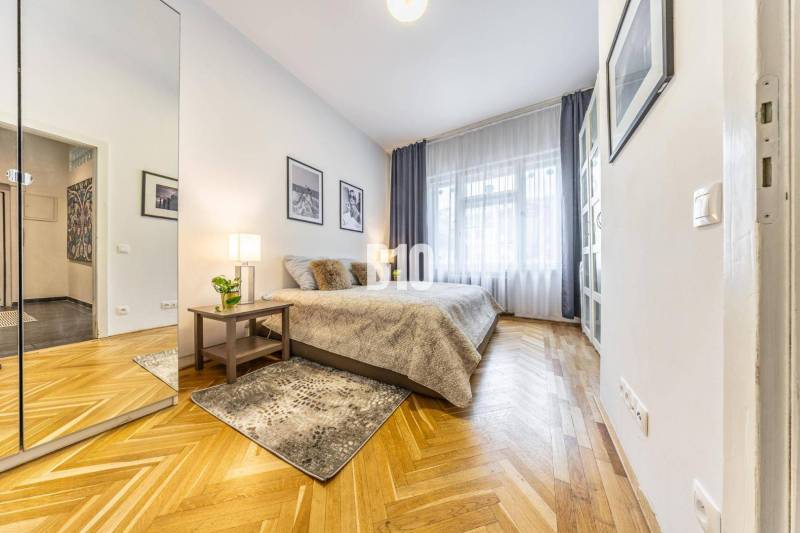 A bright room in a 2-room apartment with wooden flooring, a mirror, and decorative pictures.