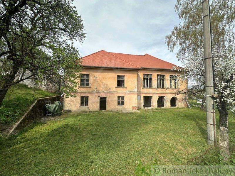 A family house in Rimavská Sobota with a red roof, situated among trees and grass.