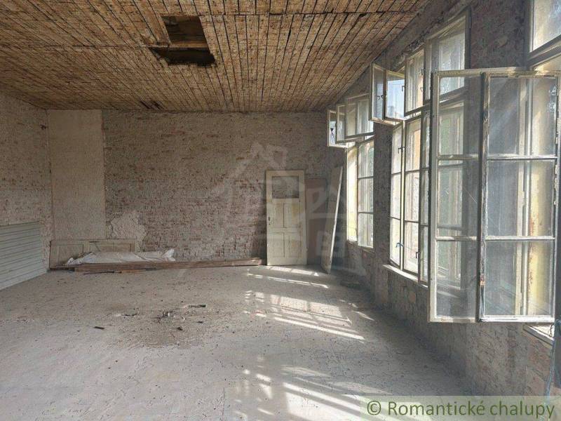 A spacious room with tall windows and a worn-out ceiling in a family house.