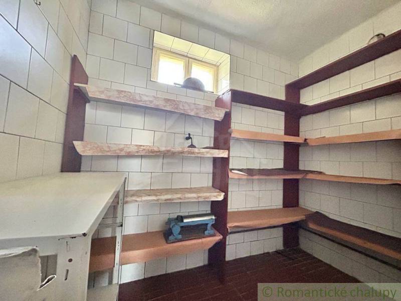 A pantry in a family house with shelves, tiled walls, a small window letting in light.