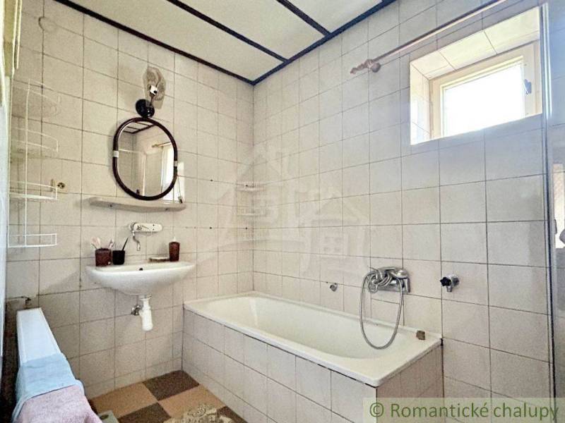 A bathroom in a family house with white tiles, a bathtub, and a sink.
